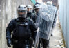 Police officers in riot gear down alleyway