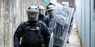 Police officers in riot gear down alleyway