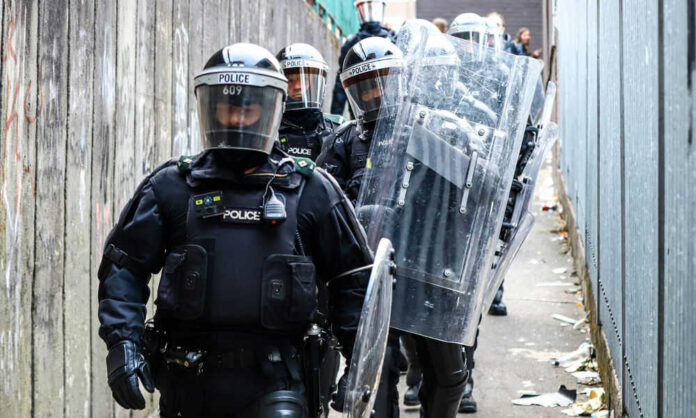 Police officers in riot gear down alleyway