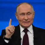 Man in suit gestures with raised index finger