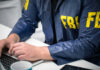 Person in FBI jacket using a laptop