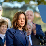 Protesters HIJACK Kamala’s Book Tour! – YIKES Woman speaking at podium with audience behind her