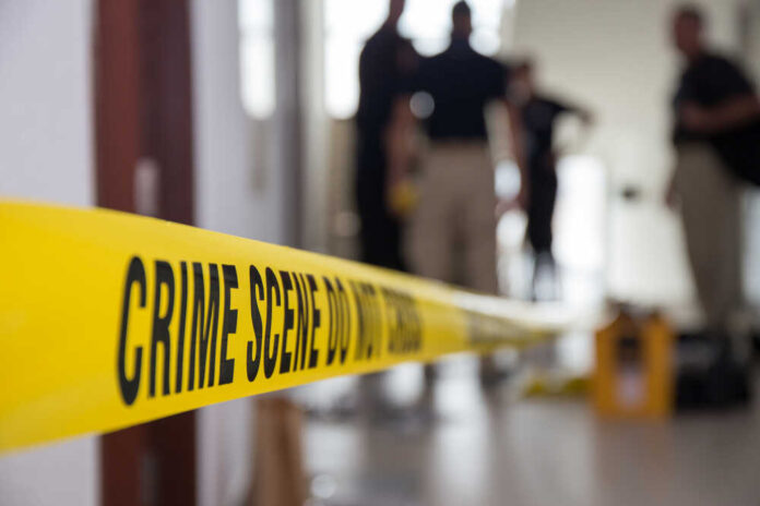 shutterstock_429955534.jpg Yellow crime scene tape with blurred figures in the background