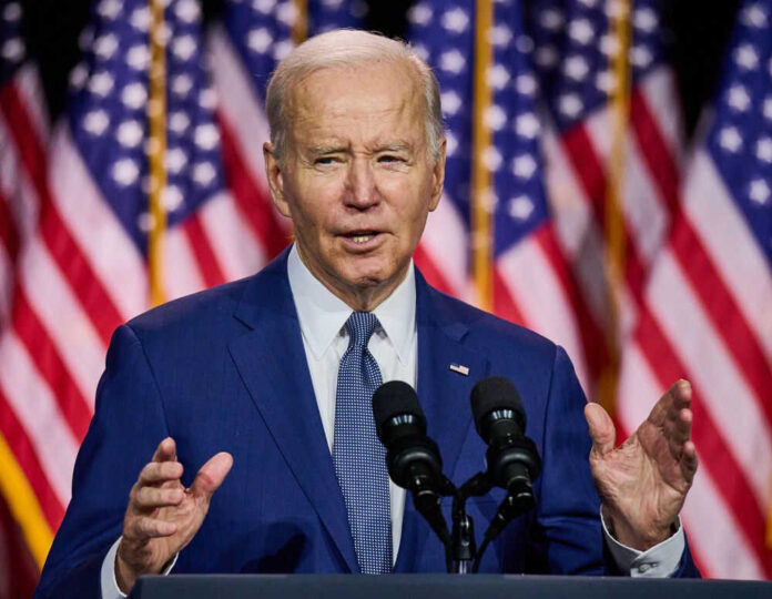 Man speaking in front of American flags and microphones
