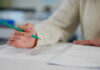Person holding pencil over exam paper on table