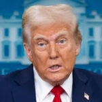 Person speaking wearing suit with American flag pin